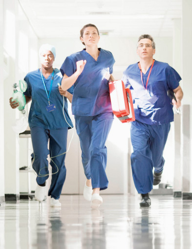 Three healthcare professionals running down a hospital hallway to treat a patient having an emergency. 